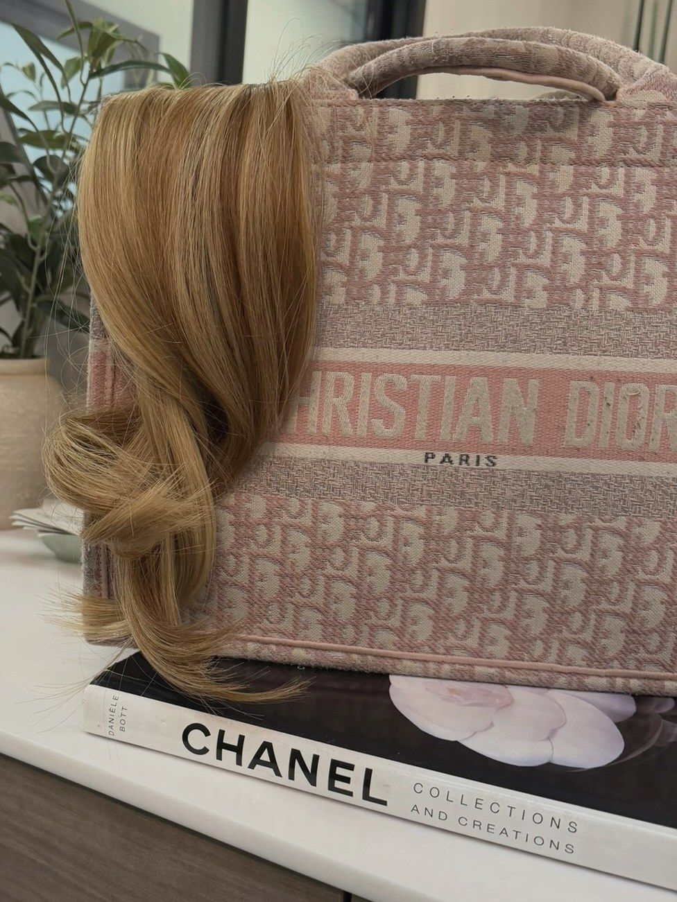 Curled hair extensions resting on a tote bag and a Chanel book